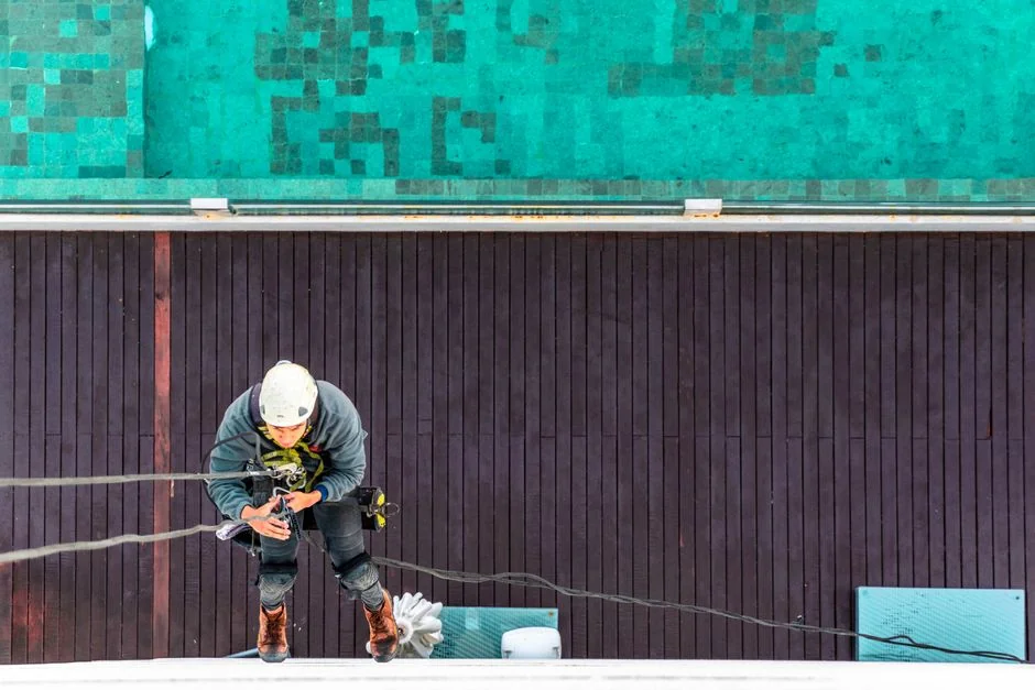 pourquoi-nous-choisir Three window cleaners suspended on ropes clean a modern glass building facade during the day.