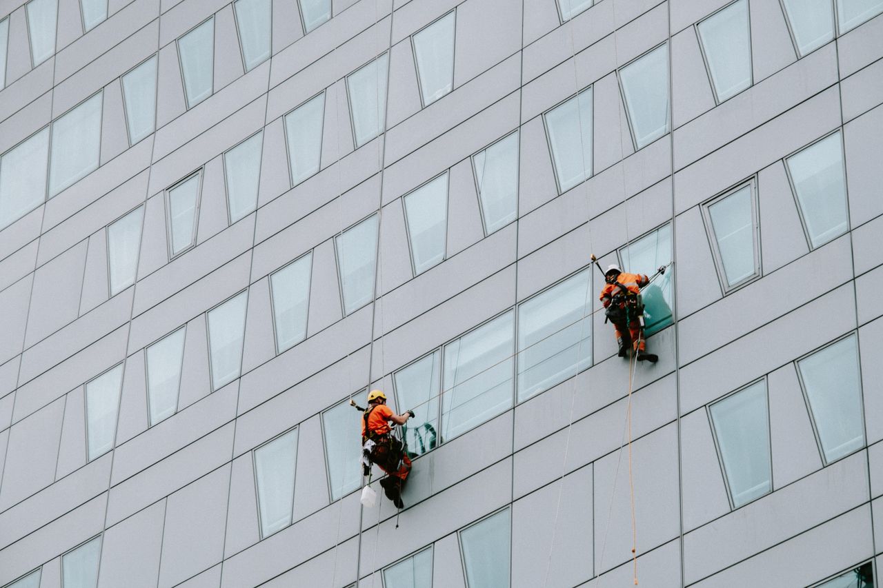 hero-img-02 Des laveurs de vitres en hauteur, équipés de protections, nettoient la façade d’un gratte-ciel.